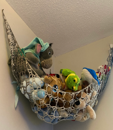 Crochet toy hammock hanging neatly with plush toys inside, showcasing a handmade storage solution pattern perfect for organizing stuffed animals in a nursery or playroom.