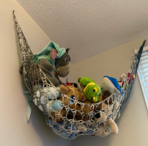 Crochet toy hammock hanging neatly with plush toys inside, showcasing a handmade storage solution pattern perfect for organizing stuffed animals in a nursery or playroom.